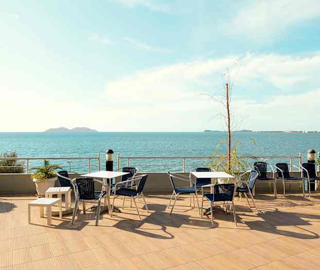 En udendørs terrasse med borde og stole og udsigt over havet. (AI-genereret tekst)