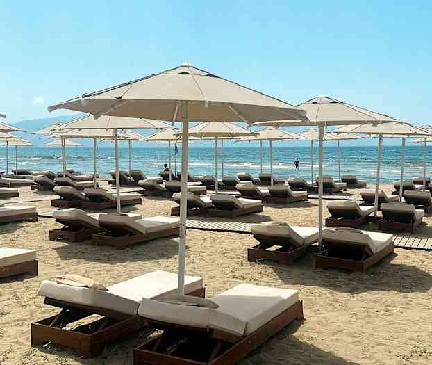 Liggestole og parasoller på en strand med havudsigt. (AI-genereret tekst)