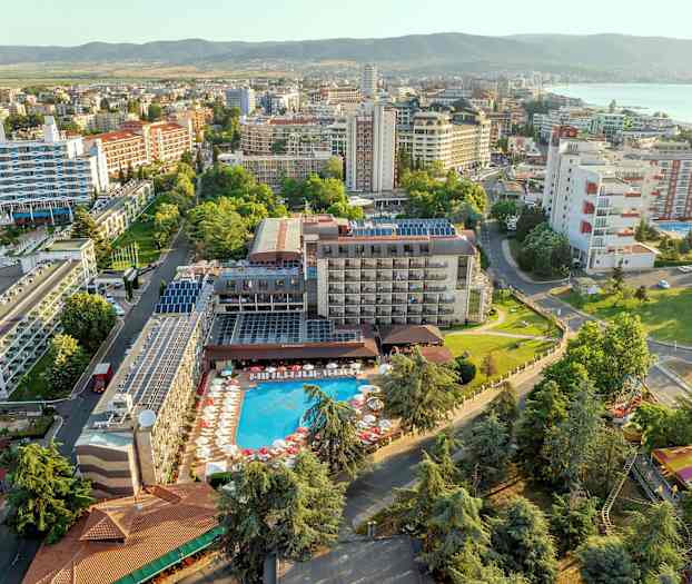 Luftudsigt over et hotel med pool og omkringliggende bygninger i et grønt område. (AI-genereret tekst)