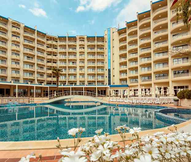 Et hotel med flere etager, der omkranser en udendørs pool og frodig have. (AI-genereret tekst)