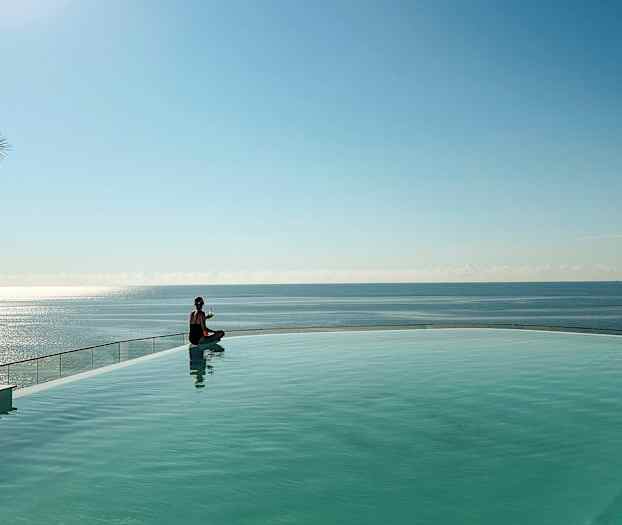 En person sidder ved kanten af en pool med havet i baggrunden. (AI-genereret tekst)