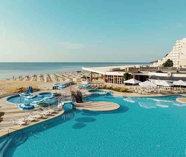 Et billede af en pool, liggestole og parasoller ved et hotel tæt på en sandstrand. (AI-genereret tekst)