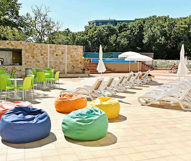 Liggestole og parasoller ved en pool, med farverige sækkestole og grønne stole. (AI-genereret tekst)