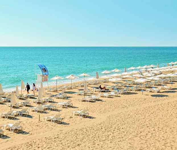 En strand med liggestole og parasoller tæt på havet. (AI-genereret tekst)