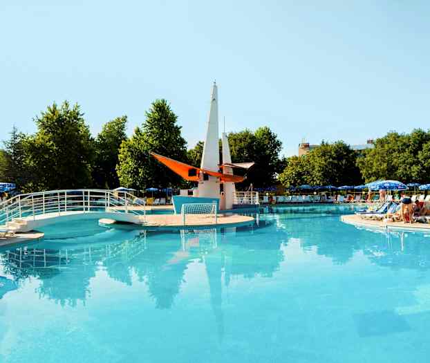 Åben pool med bro og dekorativ båd i midten, omgivet af liggestole og parasoller. (AI-genereret tekst)