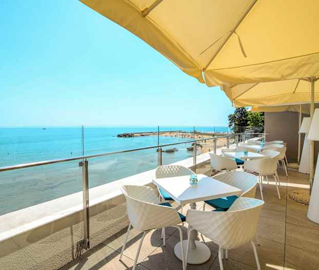 Terrasse med borde og stole under parasoller med udsigt mod stranden og havet. (AI-genereret tekst)