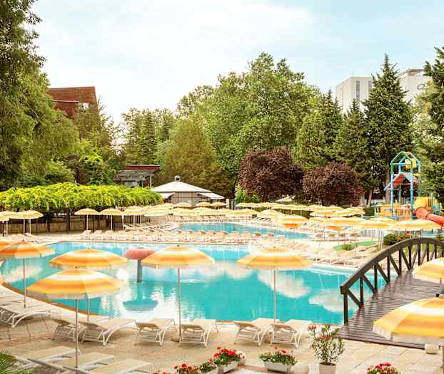 Poolområde med liggestole og gule parasoller, omgivet af grønt område. (AI-genereret tekst)