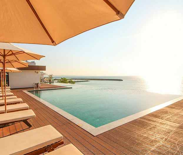 Poolområde med liggestole og parasoller med udsigt over havet. (AI-genereret tekst)