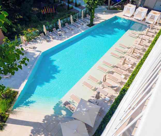 Et billede af en pool med liggestole og parasoller omkring i et udendørsmiljø. (AI-genereret tekst)