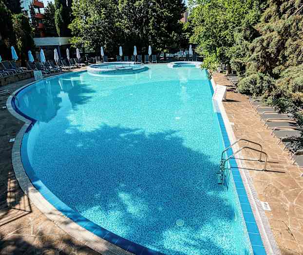 Udendørs pool omgivet af liggestole og træer. (AI-genereret tekst)