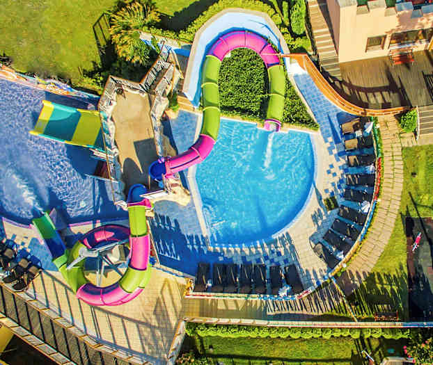 Luftfoto af en pool med rutsjebaner og liggestole omkring. (AI-genereret tekst)