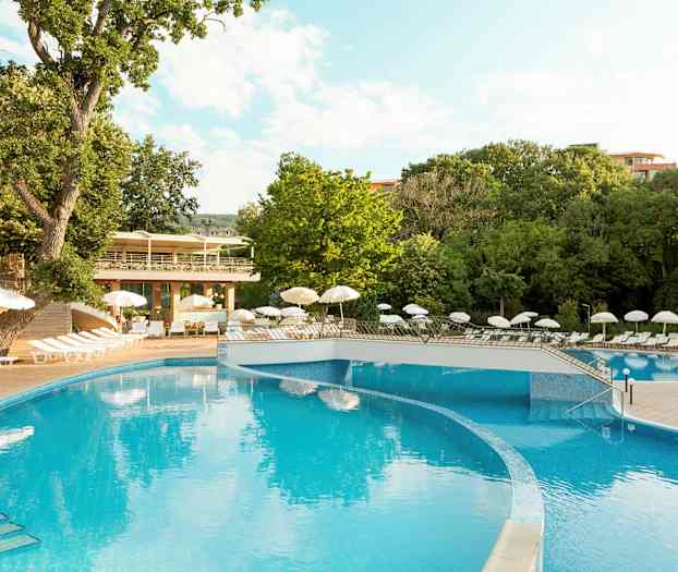 Udendørs swimmingpool omgivet af liggestole og parasoller, omgivet af grønne træer. (AI-genereret tekst)