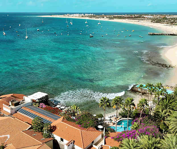 Udsigt over kysten med palmer, turkisvand og sejlbåde. (AI-genereret tekst)