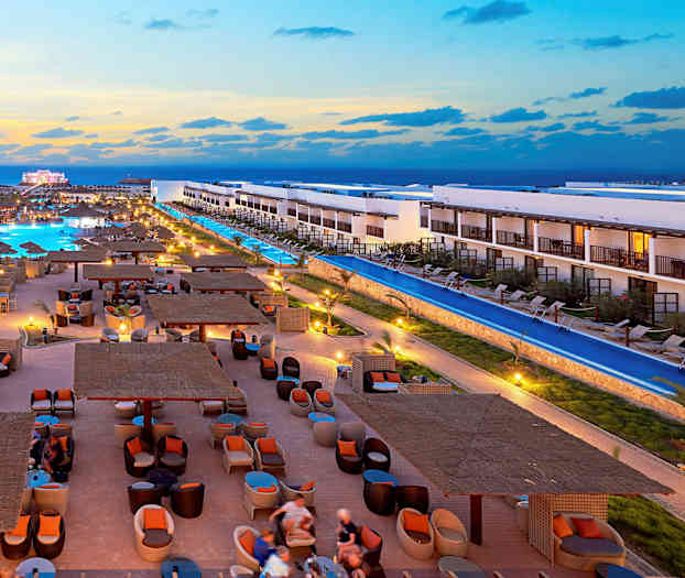 Et hotelområde med pools, elegante siddepladser og bygninger ved solnedgang. (AI-genereret tekst)