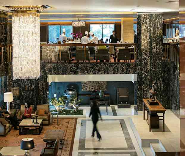 Hotellobby med elegante møbler, store vinduer og en stor lysekrone, der hænger fra loftet. (AI-genereret tekst)