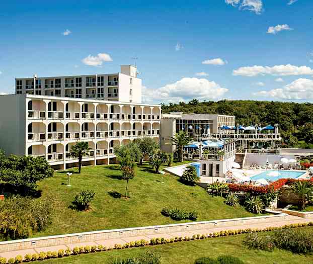 Et bygningskompleks omgivet af en velplejet græsplæne og have, med en swimmingpool og udendørs serveringsområder. (AI-genereret tekst)