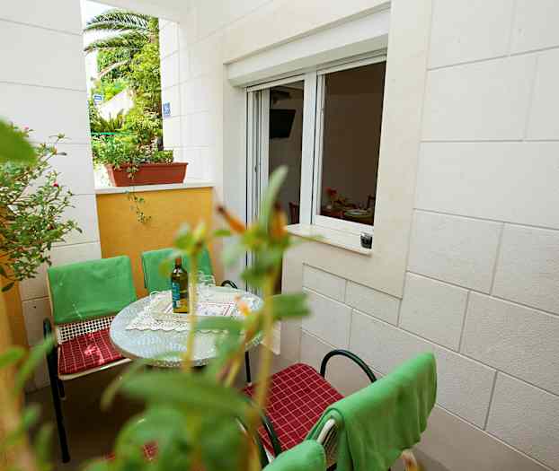 En terrasse med bord, grønne stole og vindue til et rum. (AI-genereret tekst)