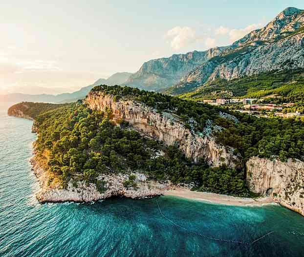 En kystlinje med bratte klipper, en skov og klart blåt hav. (AI-genereret tekst)