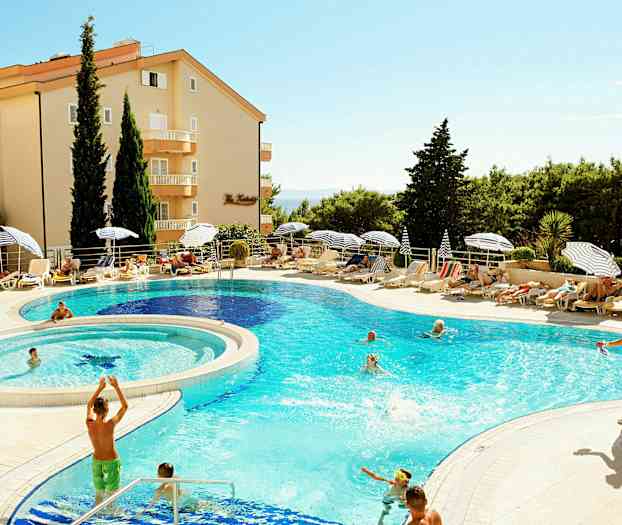 Et feriested med en pool omgivet af liggestole, parasoller og grønne træer. (AI-genereret tekst)