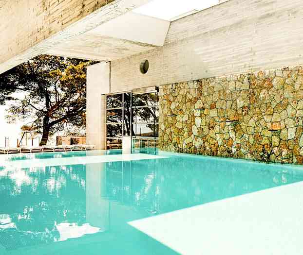 Indendørs pool med stenmur og udsigt til træer udenfor. (AI-genereret tekst)