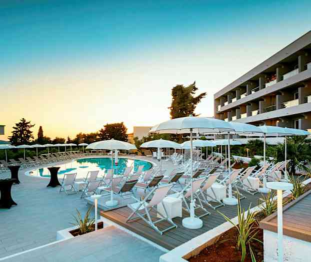 Et hotelpoolområde med liggestole og parasoller i skumringen. (AI-genereret tekst)