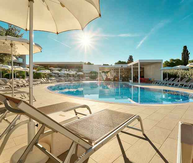 En udendørs swimmingpool omgivet af liggestole og parasoller under en klar blå himmel. (AI-genereret tekst)