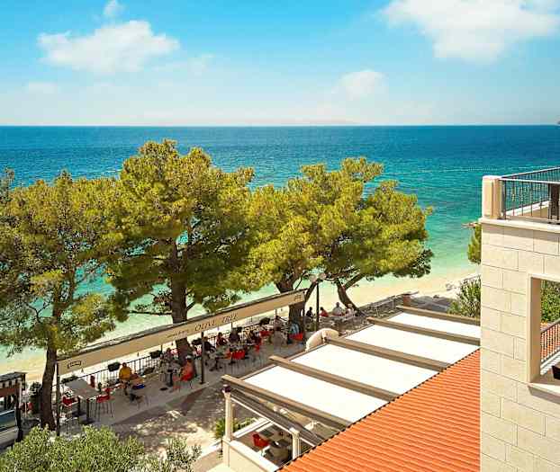 Udsigt over en restaurant ved stranden med havet i baggrunden. (AI-genereret tekst)