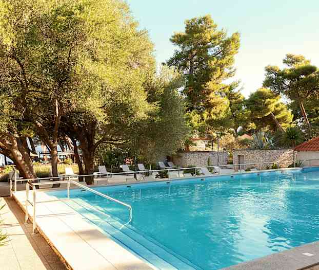 En udendørs pool omgivet af træer og liggestole. (AI-genereret tekst)