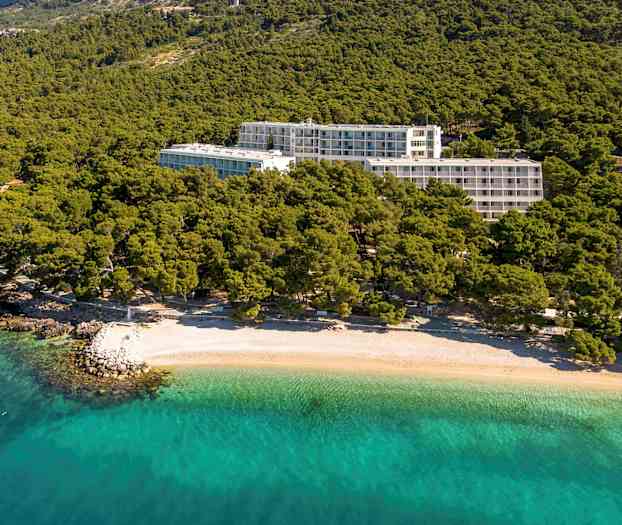 Hotelbygninger omgivet af grønt nær en strand med klart turkis vand. (AI-genereret tekst)