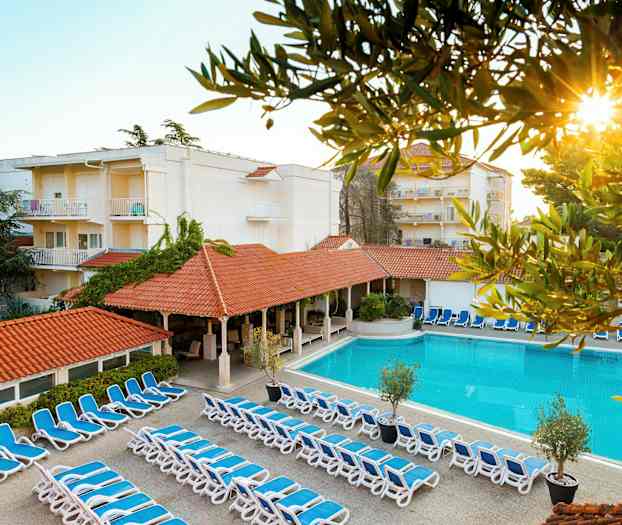 Billede af hotelområde med liggestole, pool og bygninger. (AI-genereret tekst)