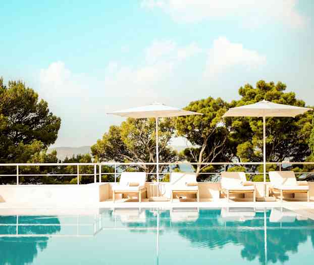 En udendørs pool omgivet af liggestole, parasoller og frodige træer. (AI-genereret tekst)