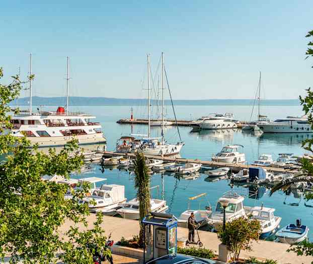 En marina med sejlbåde og motorbåde. Nogle mennesker står på broerne. (AI-genereret tekst)