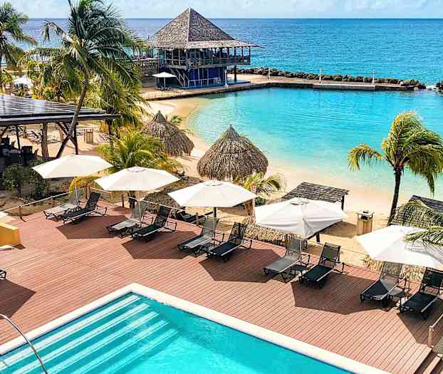 Udsigt over en strand med liggestole, parasoller, palmer og en pool. Havet er synligt i baggrunden. (AI-genereret tekst)