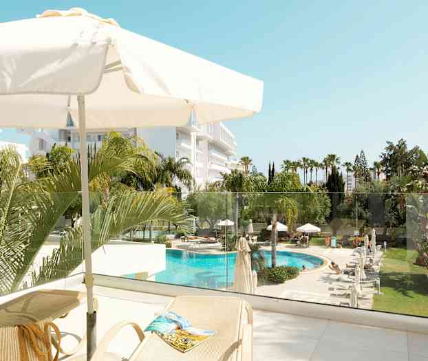 Udsigt fra en terrasse med parasol, liggestole og udsigt over en pool og have. (AI-genereret tekst)