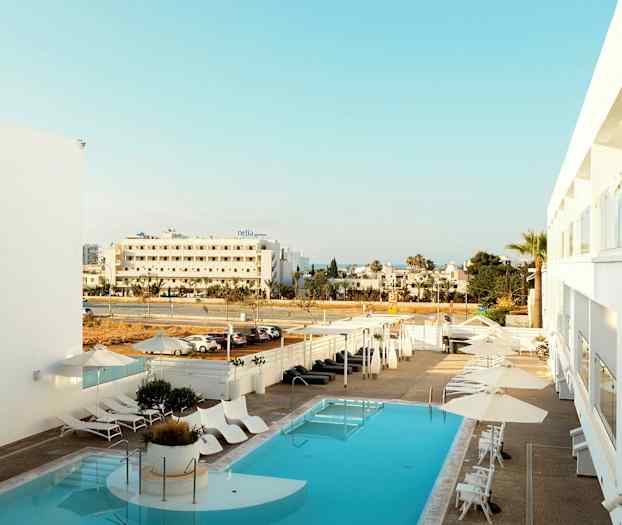 Hotel pool med liggestole og parasoller, udsigt til gaden og de omkringliggende bygninger. (AI-genereret tekst)