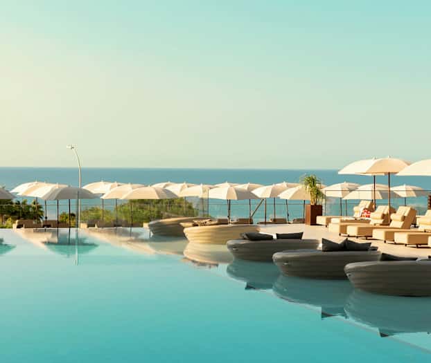 En infinitypool med liggestole og parasoller ved havet. (AI-genereret tekst)