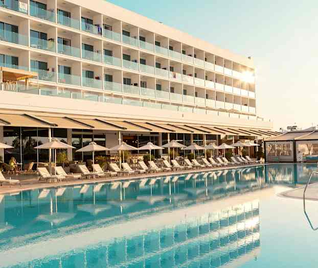 En hotelbygning med altaner ses bag en pool og liggestole. (AI-genereret tekst)