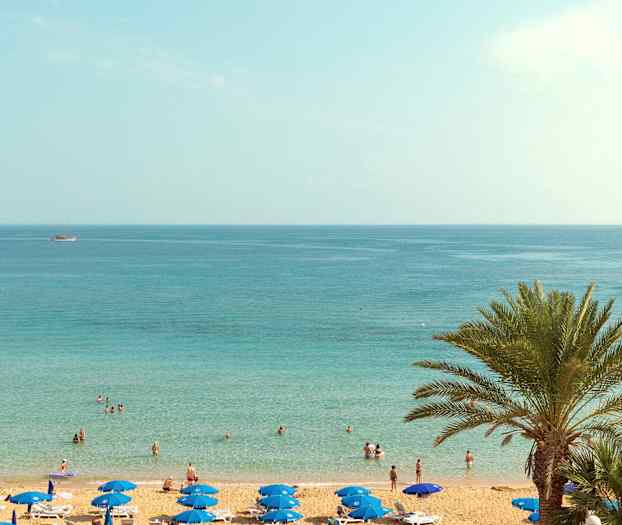 En strand med parasoller og mennesker ved vandet. (AI-genereret tekst)