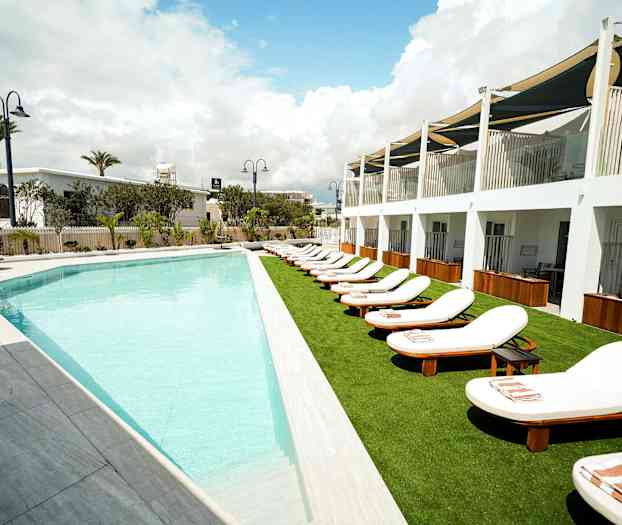 Udendørs pool med liggestole ved en hotelbygning. (AI-genereret tekst)