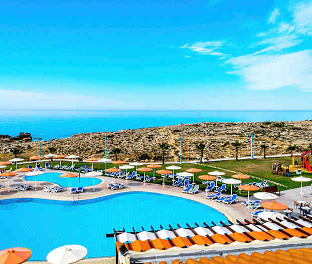 Udsigt over en pool med liggestole og parasoller, mod havet og klippefulde landskab. (AI-genereret tekst)