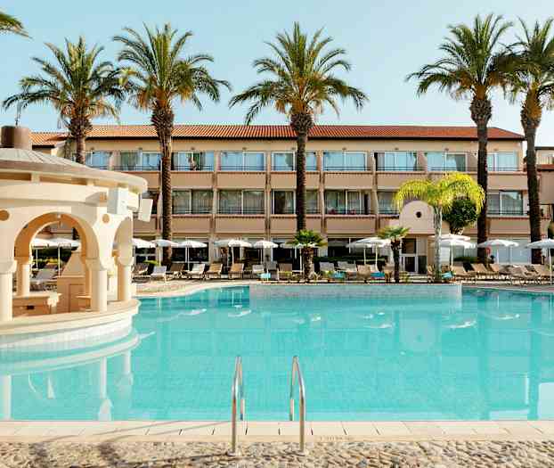 Billede af et hotel med udendørs swimmingpool og omgivende liggestole og parasoller. (AI-genereret tekst)