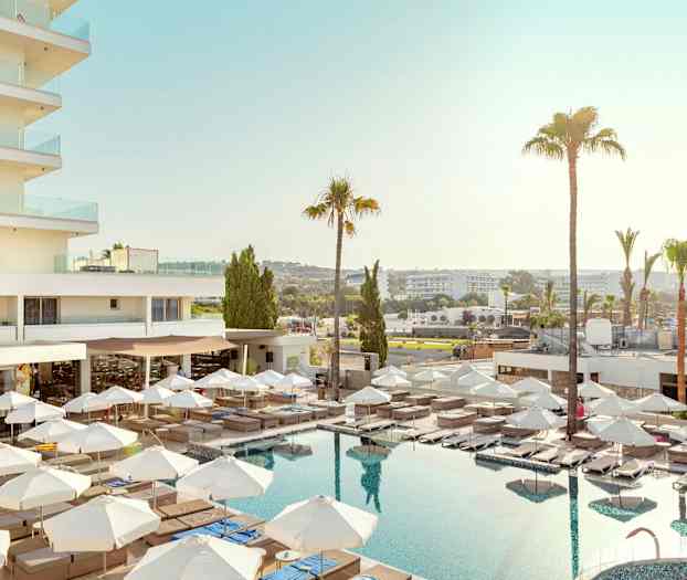 Hoteludsigt med pool, liggestole og parasoller. (AI-genereret tekst)