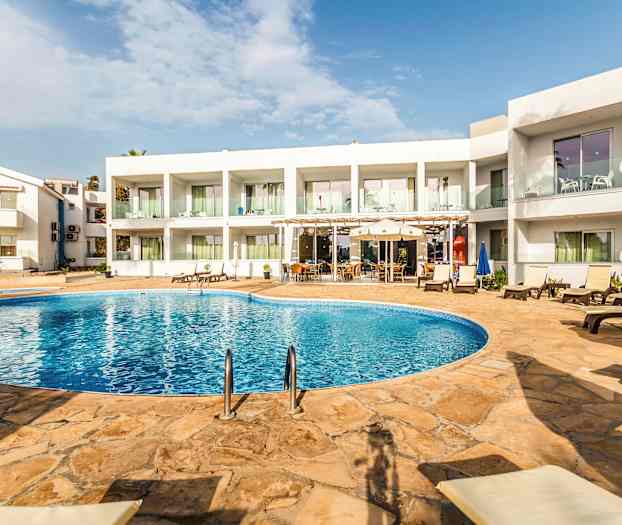 En hotelpool med liggestole og borde i et område omgivet af hvidmalet bygning. (AI-genereret tekst)