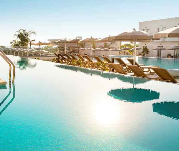 En udendørs pool med liggestole og parasoller langs kanten. (AI-genereret tekst)