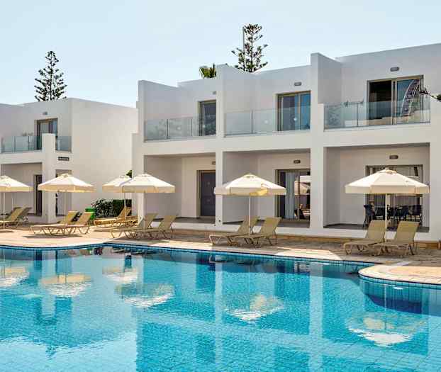 Hvidmalede bygninger med terrasser ved poolområde med liggestole og parasoller. (AI-genereret tekst)