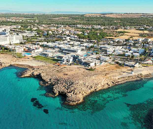 Luftfoto af kystlandskab med turkisblåt vand og bygninger ved stranden. (AI-genereret tekst)