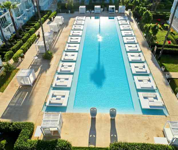 En rektangulær pool omgivet af liggestole og grønne områder. (AI-genereret tekst)