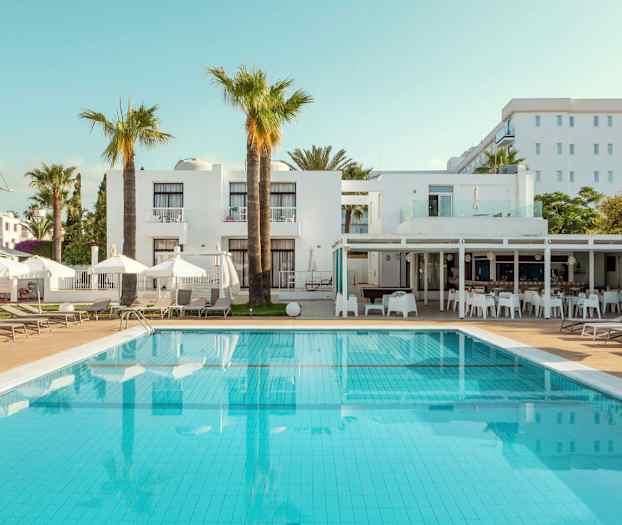 Billede af hotelpool med liggestole og hvide bygninger i baggrunden. (AI-genereret tekst)