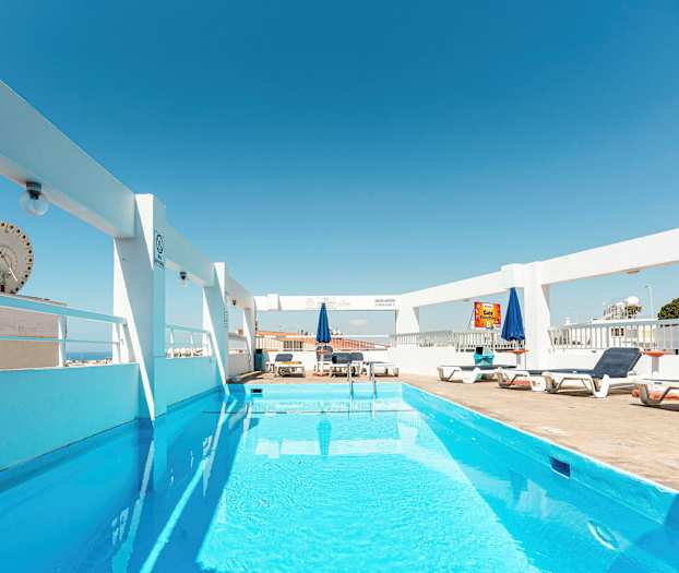 En udendørs pool med liggestole og parasoller under en klar blå himmel. (AI-genereret tekst)