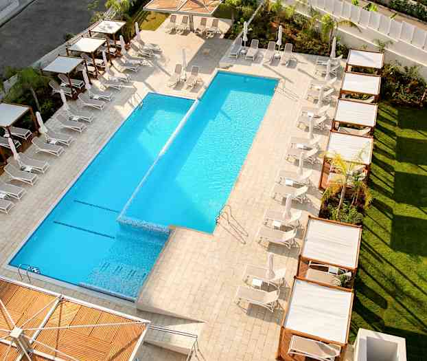 Udsigt over en udendørs pool omgivet af liggestole og skyggegivende pergolaer. (AI-genereret tekst)